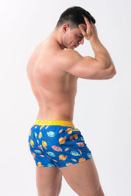 Short de bain Playo Fish en polyester 100 % bleu avec motif coloré de poissons tropicaux, bordé de passepoil jaune. Conçu pour un porté confortable, il possède une taille élastique avec cordon de serrage et une doublure en maille intérieure. Parfait pour la plage ou la baignade.
