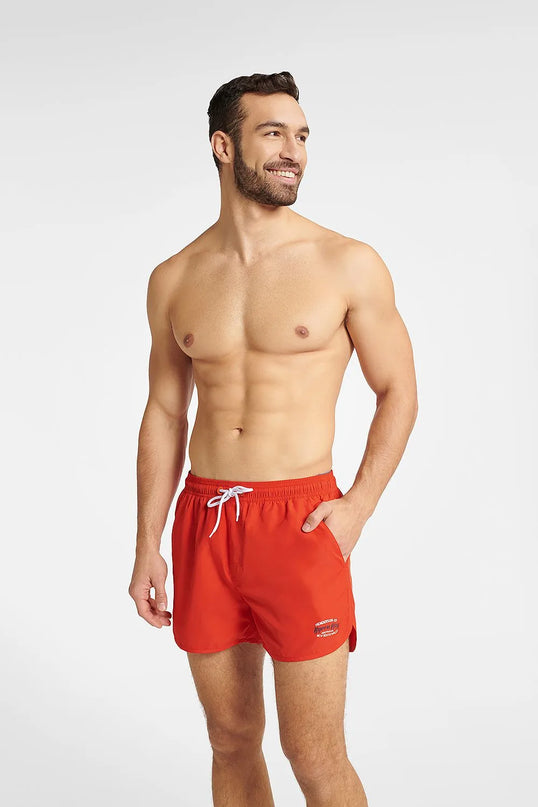 Homme portant un short de bain rouge GUILD à séchage rapide, avec une taille élastique réglable et des détails contrastés. Modèle confortable et tendance, idéal pour la plage et les activités aquatiques. Disponible en tailles M, L, XL, XXL.