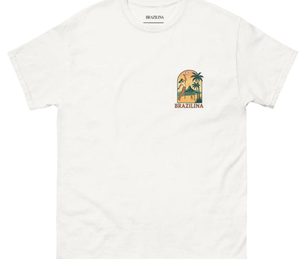 T-shirt blanc au design inspiré du Brésil avec un motif tropical représentant une figure dynamique devant des palmiers et un coucher de soleil. Le mot 'Brazilina' est inscrit en dessous du logo, évoquant la culture et l'atmosphère festive des plages brésiliennes.