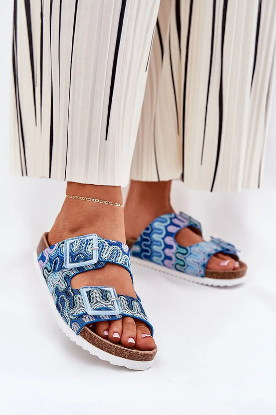 Sandales pour femmes sur plateforme en liège, avec motifs colorés en tissu textile, deux brides à boucles décorées de paillettes, semelle intérieure en cuir suédé, parfaites pour l'été. Présentées portées avec un pantalon blanc à rayures noires.