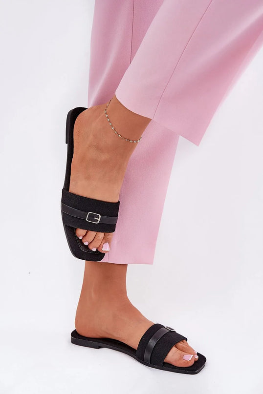 Sandales plates pour femmes en matériau textile noir, dotées d'une fine bride avec boucle décorative à l'avant, portées avec un pantalon rose. Idéales pour l'été, elles offrent confort et style avec une semelle de 1 cm en cuir écologique et tissu, parfaites pour les tenues légères.