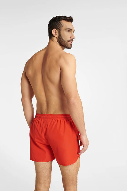 Homme portant un short de bain rouge énergique GUILD à séchage rapide, coupe ample avec taille élastique ajustable, idéal pour la plage et les activités aquatiques.