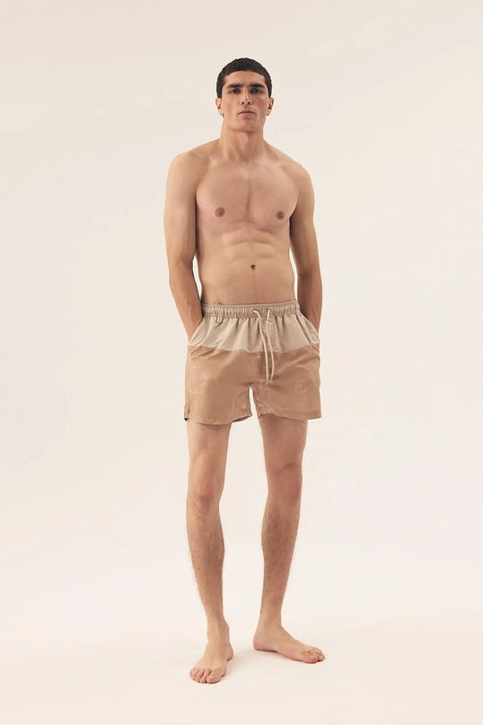 Short de bain homme beige inspiré du style brésilien, évoquant les plages tropicales et la nature luxuriante, avec une coupe décontractée et élégante. Parfait pour les journées en bord de mer, conçu avec des motifs subtils qui rendent hommage à la culture festive et ensoleillée du Brésil.