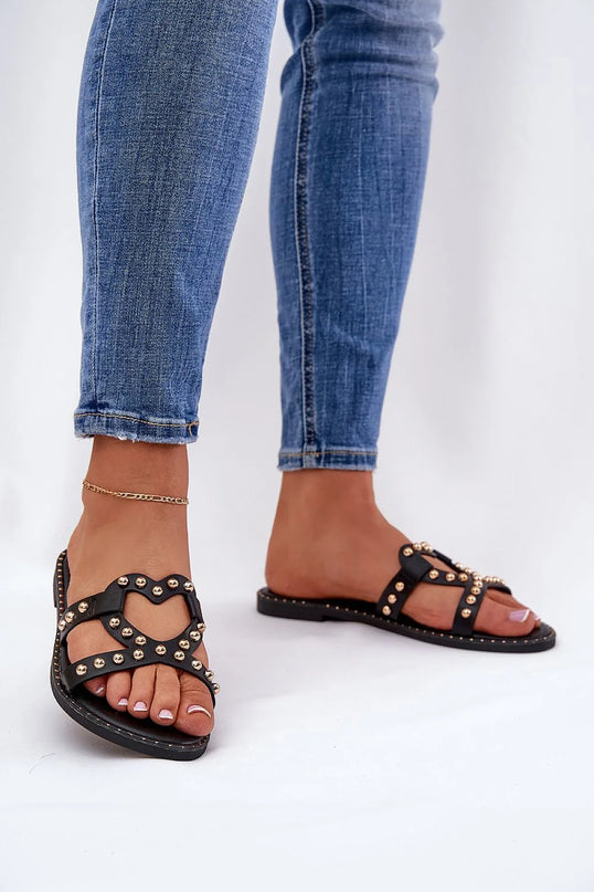 Sandales femme noires inspirées de la mode brésilienne, ornées de détails métalliques dorés et au design audacieux, évoquant l'esprit festif des plages du Brésil. Idéales pour les promenades estivales avec une touche élégante et décontractée, portées ici avec un jean ajusté.