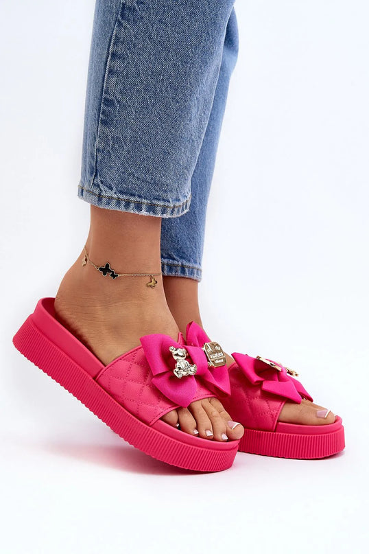 Claquettes pour femmes en simili cuir rose avec plateforme massive de 4,5 cm, ornées d'un nœud en tissu rose et d'un fermoir décoratif avec un ours en peluche argenté et une plaque dorée. Chaussures élégantes et tendance, parfaites pour la saison estivale.