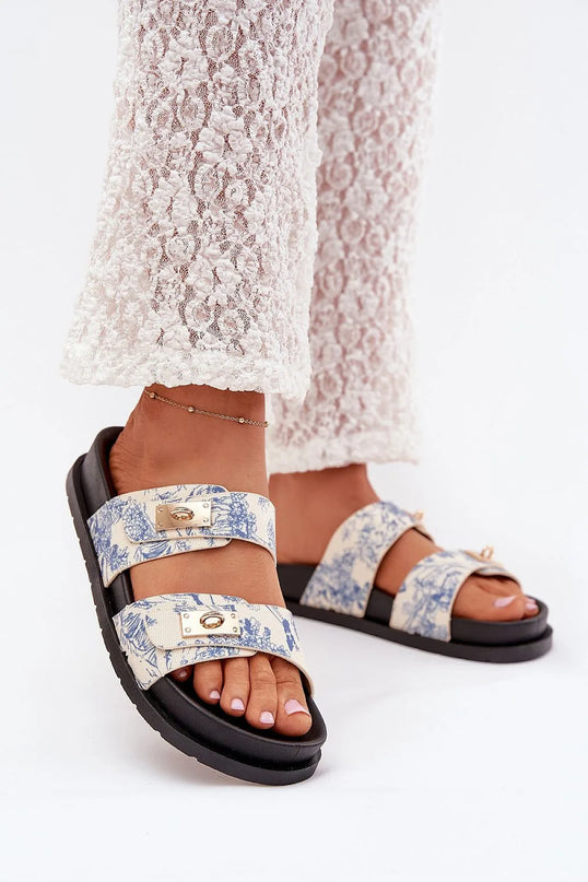 Sandales d'inspiration brésilienne, avec des motifs tropicaux bleus sur fond beige, deux brides ajustables avec détails dorés, semelle noire confortable, idéales pour un style chic et décontracté en été.