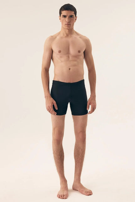 Homme portant un short de bain noir minimaliste et élégant pour homme, conçu avec une longueur de jambe moyenne. Le short est fabriqué en tissu lisse et à séchage rapide, idéal pour la plage ou les activités aquatiques. Modèle sans poches, avec taille à lacets pour un ajustement parfait, photographié sur un fond neutre.